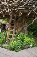 Photographer: Annaick Guitteny -The RHS Back to Nature Garden, view of the treehouse which is underplanted with ferns, Dryopteris filix-mas and Athyrium filix-femina,  Luzula nivea, Lamium and Vinca. RHS Chelsea Flower Show 2019.