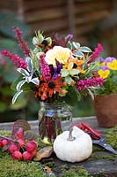 Posy or Tussie Mussie with a colourful  mix of flowers and foliage on table with Malus - Crabapple - fruits, moss and white Winter Squash