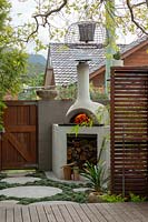 A bespoke cement rendered pizza oven in the back corner of a backyard.