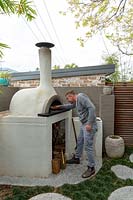 Man putting firewood into a bespoke cement rendered pizza oven.