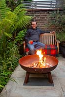 Justin Edwards sitting by a fire pit in his green oasis garden in West London.