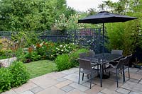 Contemporary garden in West London - view from stone paving patio with table and parasol through borders with Verbena bonariensis, Echinacea Magnus Superior, Helenium Moerheim Beauty, towards artificial lawn.