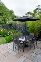 Contemporary  garden in West London - view from stone paving patio with table and parasol through borders with Verbena bonariensis, Echinacea Magnus Superior, Helenium Moerheim Beauty, towards artificial lawn.