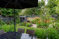 Contemporary garden in West London - view from patio with table and parasol through borders with Verbena bonariensis, Echinacea Magnus Superior, Helenium Moerheim Beauty, towards artificial lawn.
