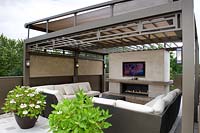 Flat screen television showing London 2012 Olympic Games, above modern outdoor fire pit in contemporary, urban town roof garden.