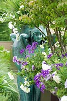 View past Euonymus, underplanted with flowering Petunia and Verbena to statue of woman. 