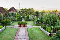 View down central axis of kitchen garden taking in metal sculpture and arch beyond. Each quarter has an area of lawn with large raised bed edged with railway sleepers and full of crops