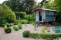 Traditional gypsy caravan stationed in gravel garden with sparse planting