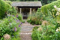 The herb garden with clipped yew spheres around a central circle set with a mill stone, and lush planting including fennel, alliums and verbena with slate roofed summerhouse at the end in July. York Gate Garden, Adel.