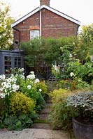 Small garden, view from paved patio along path with flower beds either side. Planting includes: Phlox 'David', Achillea 'Moonshine', Stipa arundinacea and Alchemilla mollis. Other features include: painted summerhouse, obelisk, tree in large pot and trompe l'oeil of mirror and trellis