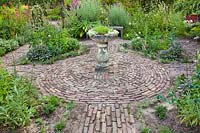 Herb garden with beds around a circular brick paved area with central stone bird bath in herb garden