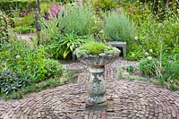 Herb beds around a circular brick paved area with central stone bird bath planted up 