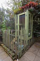 A homemade chicken coop built from second hand buliding materials, with a fence made from upturned tomato stakes and a rooftop garden planted with bromeliads.
