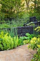 Burnt oak timbers surrounded by mixed foliage planting in woodland garden.  RHS Chelsea Flower Show 2019 