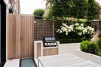 BBQ area with built in storage cupboards in cedar wood. Raised beds with Hydrangea 'Annabelle' and pleached Carpinus betulus
