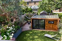 London contemporary garden - high view of garden from top floor looking down to artificial lawn with sun lounger, garden room or gym and lower wood deck area.