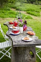 Rustic wooden table and chairs, table set for breakfast - fire place with cooking facilities in background.