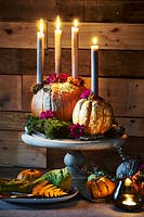 Atmospheric arrangement with candles, pumpkins and flowers on a wooden stand.