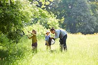 Father and children with nets trying to catch insects in meadow.