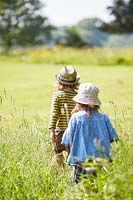 Two young children walking through meadow.