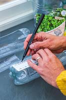 Woman using a ruler to draw an opening in plastic bottles.