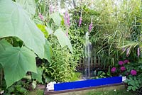 Water feature in small urban garden full of exotics. Planting includes Paulownia tomentosa, Lythrum salicaria, Bamboo, Hydrangea and Trachycarpus fortunei