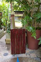 Water feature in a small town garden with tropical foliage plants including Monstera deliciosa - Swiss Cheese Plant