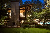 Contemporary house and garden, with trees and outdoor living area, lit up at night