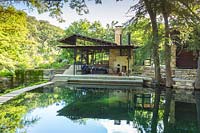 View across creek to terrace and outside seating area at Mill Creek Ranch in Vanderpool, Texas designed by Ten Eyck Landscape Inc, July.