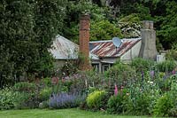 A herbaceous perennial border, in front of house with dense planting of trees beyond