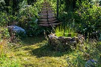 Sculptural bespoke garden chair made from recycled wood and metal, and drystone fire pit in a wild garden. Calm amidst Chaos. RHS Hampton Court Palace Flower Festival, 2019.  