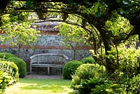 View to wooden bench from pergola, covered with trained apples in the Tunnel Garden at Heale Garden, Wiltshire, UK. 