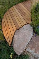 Detail of edging of a curved timber boardwalk that has been cut to conform to the shape of a rustic sandstone rock path.