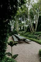 View from under yew arch in Jardin d'Aval with table and benches by German sculptor Thomas RÃ¶sler surrounded by Muehlenbeckia complexa and Ilex aquifolium. Les Jardins d Etretat, Normandy, France