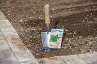 Trowel, seeds and label ready in prepared seedbed to sow  seeds