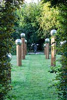 Avenue in The Meadow. Stainless steel mirror globes on top of wooden pillars of irregular height. Mobiles sculpture at the focal point is 'Octo' by Stuart Stockwell. Veddw House Garden, Monmouthshire, Wales, UK. 