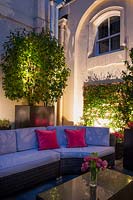 Outdoor seating area enclosed by walls, uplights to emphasis plantings of Camellia and Trachelospermum jasmonoides in large black containers