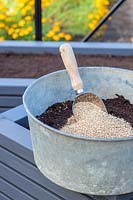 Metal tub with compost and vermiculite ready for mixing with scoop, seed sowing mix