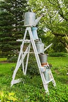 Vintage white painted wooden stepladder decorated with metal watering cans in residential garden