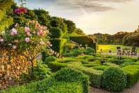 The last rays of sunlight glance across the knot garden with its climbing rose in the foreground, and the main lawn and Topiary Forest of clipped yew and box - Taxus baccata, Buxus sempervirens in the background. The sun drops behind the woodland shelter belt beyond. This image was runner-up in the Celebrating Gardens category of the annual RHS Photographic Competition.