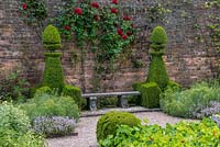 The Herb Garden. A bench flanked by box topiary, in a small formal walled garden.