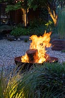 A blazing fire pit on gravel in a contemporary courtyard garden.