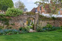 Ancient walls contain a walled garden, view through arch to period house beyond