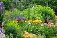 Colourful border with metal oblisks. Plants include Hemerocallis, Helenium, Veronicastrum, Rudbeckia hirta 'Cappuccino', and Echinops.