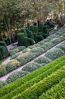 View over terraced pathways and sculpted Box and Eleagnus hedges to a group of shaped yew columns and arches.