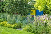 Summer borders with  Mondrian inspired painted wall in the background Planting includes Miscanthus sinensis 'Morning Light'