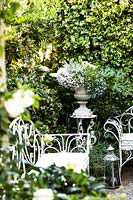 White metal benches in courtyard garden with classic urn container