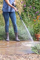 Woman using pressure washer to clean circular patio