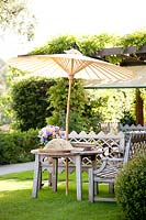 Wooden table, parasol and benches in lawn in Italian garden.
