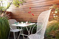 White table and chairs set with tableware in modern, terrace garden. 
